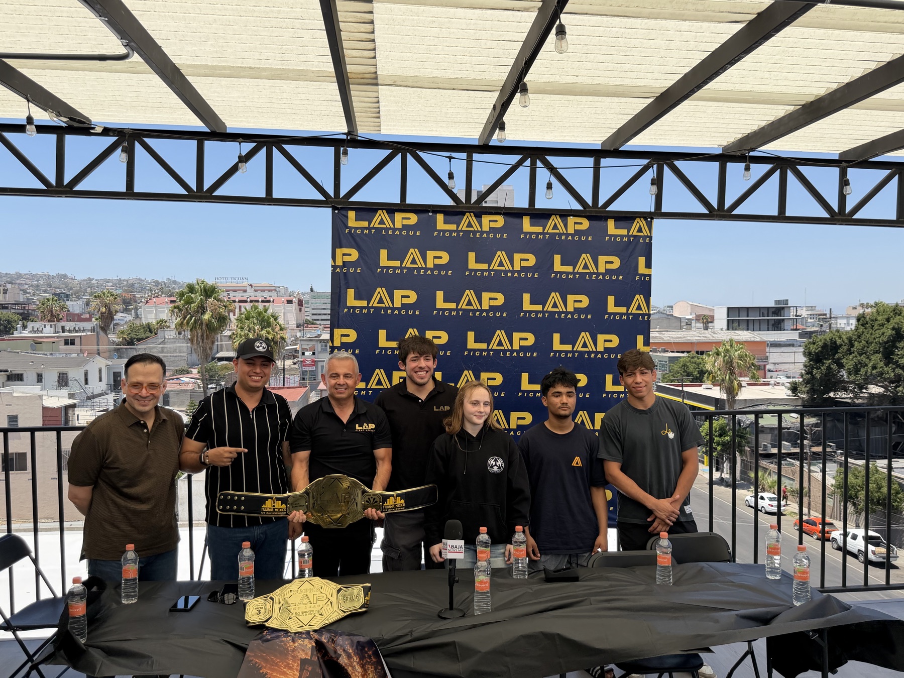 Emma Chandler, center in black, with LAP Fight League organizers and fellow card fighters at the LAP 06 press conference in Tijuana, the championship belt on the table.